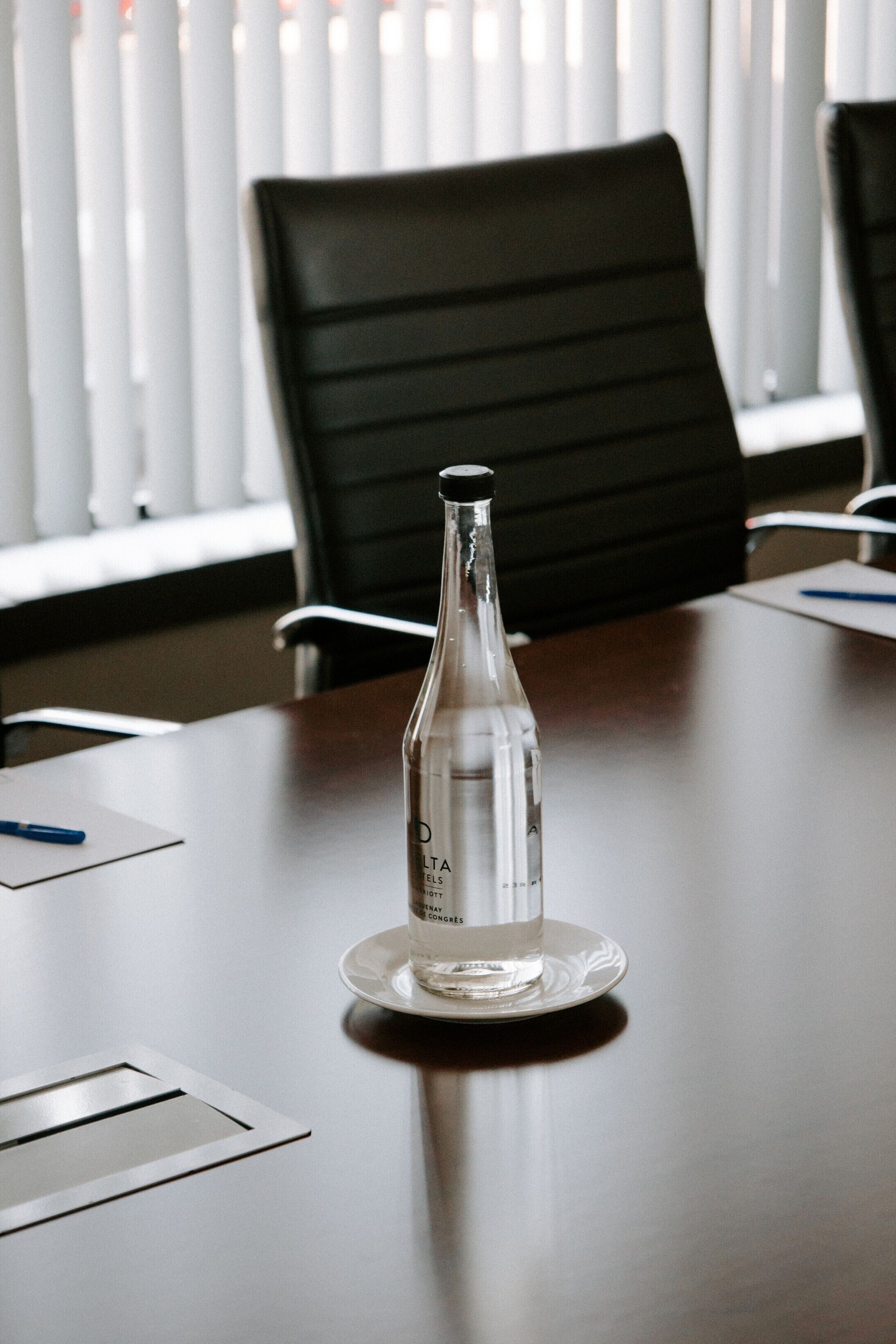 Una mesa de conferencias con una botella transparente sobre un plato, un bolígrafo y documentos.