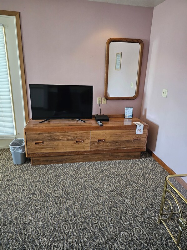 A wooden console bed with a flat-screen TV, a remote, and a small table with a phone and a sign.