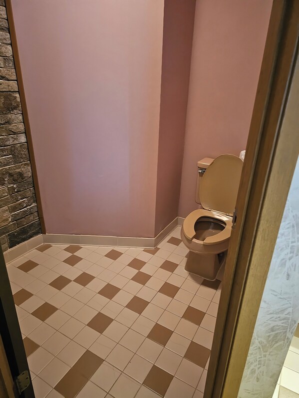 Un baño con inodoro, paredes rosadas y piso a cuadros.