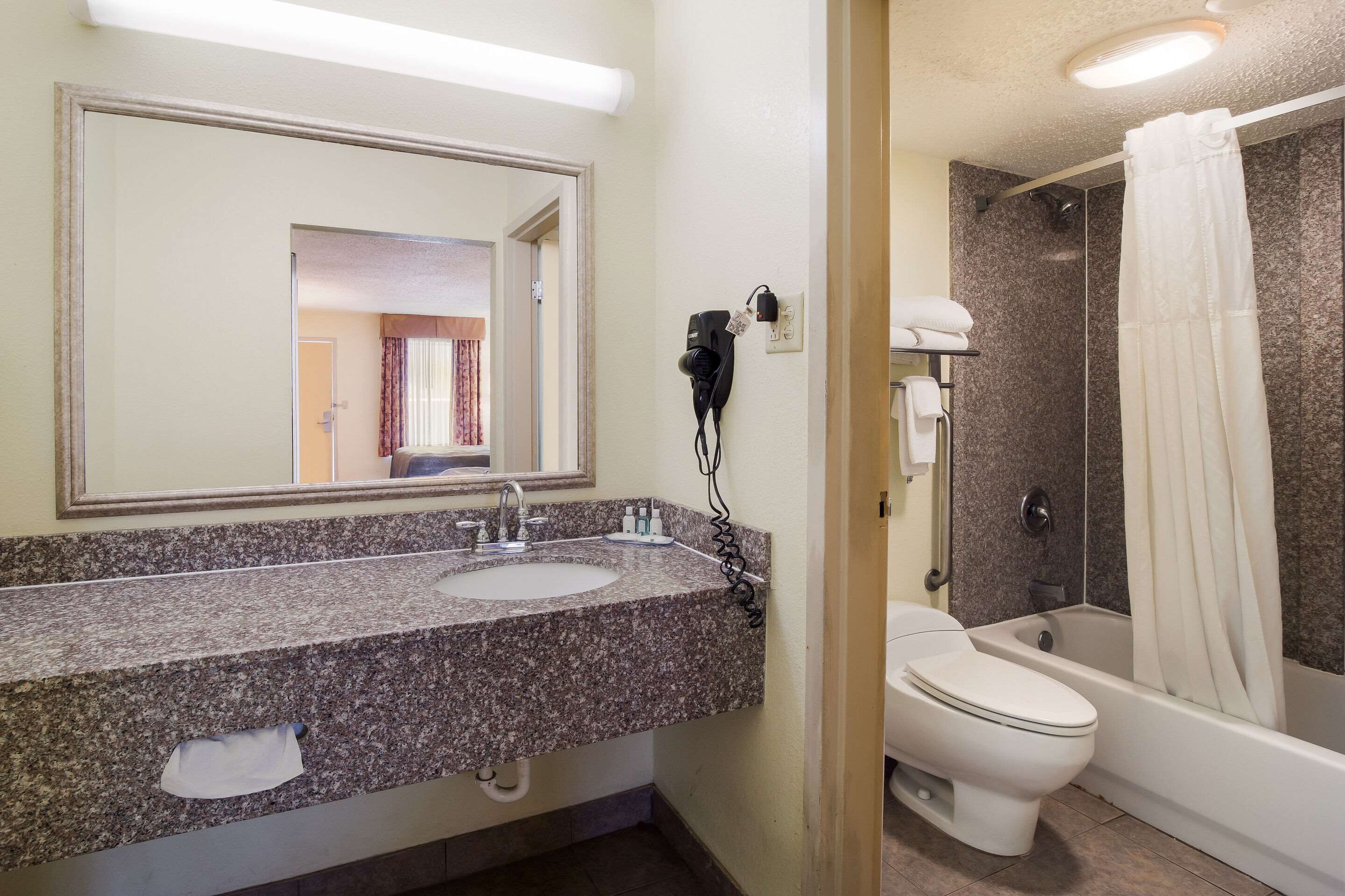 Baño con lavamanos de granito, espejo, secador de pelo, inodoro y ducha con cortina.