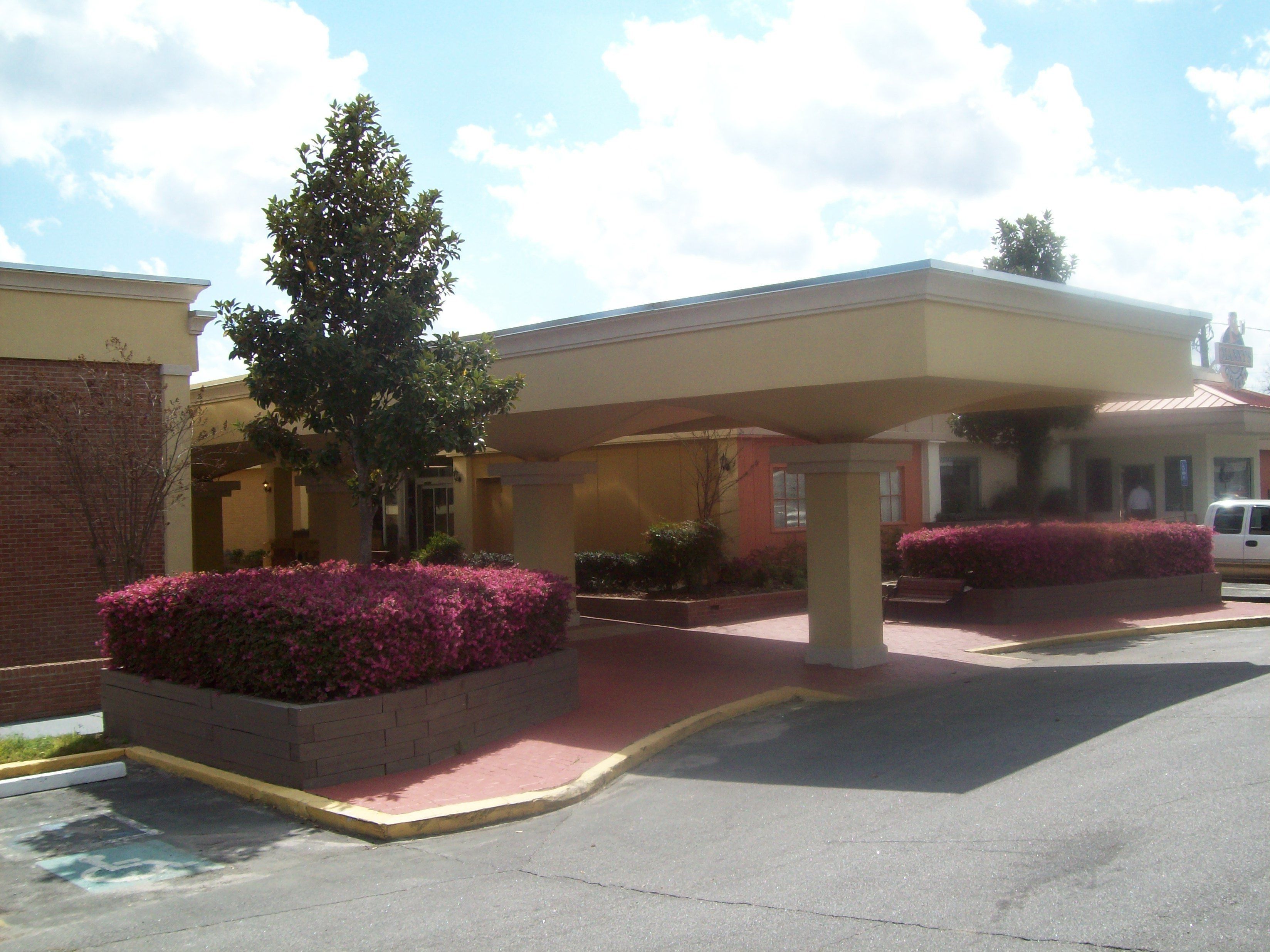 A hotel entrance with a covered walkway, brick walls, and landscaped flower beds.