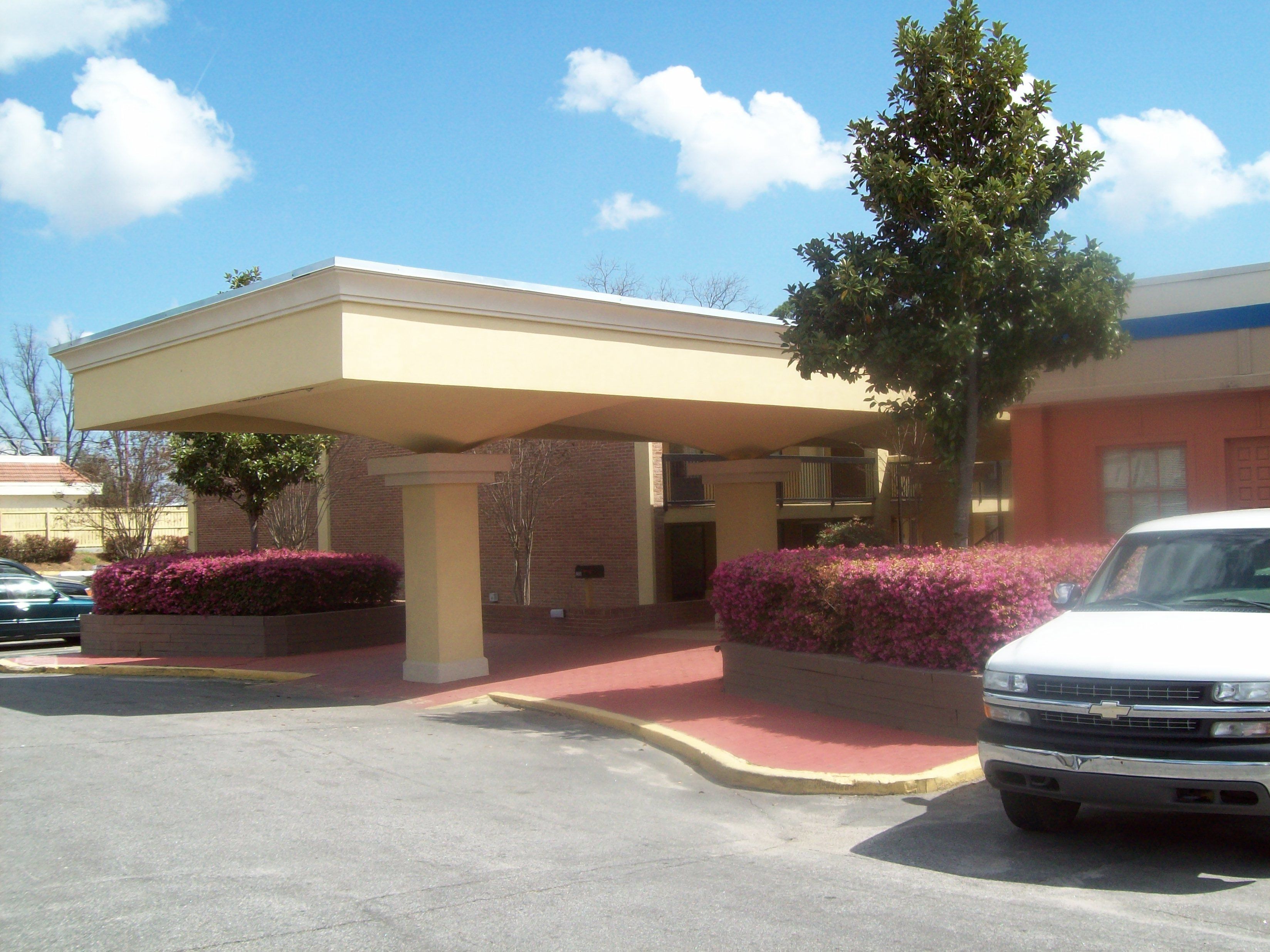 A hotel entrance with a covered walkway, brick walls, and a parking lot.