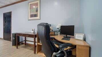 A hotel room with a wooden desk, a black office chair, a computer, and a framed picture on the wall.