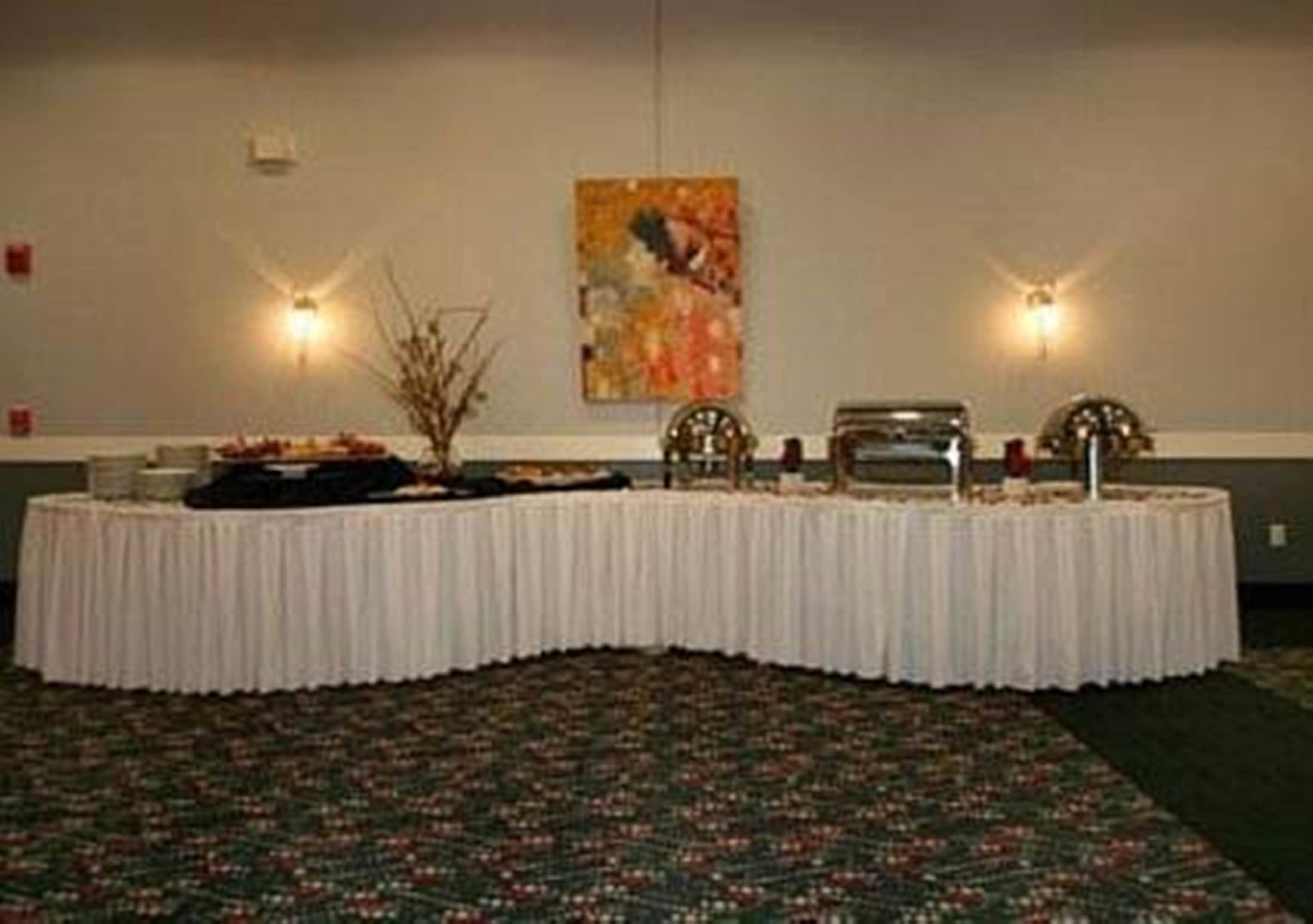 A conference room with a round table covered by a white tablecloth, two wall-mounted lamps, and a painting on the wall.