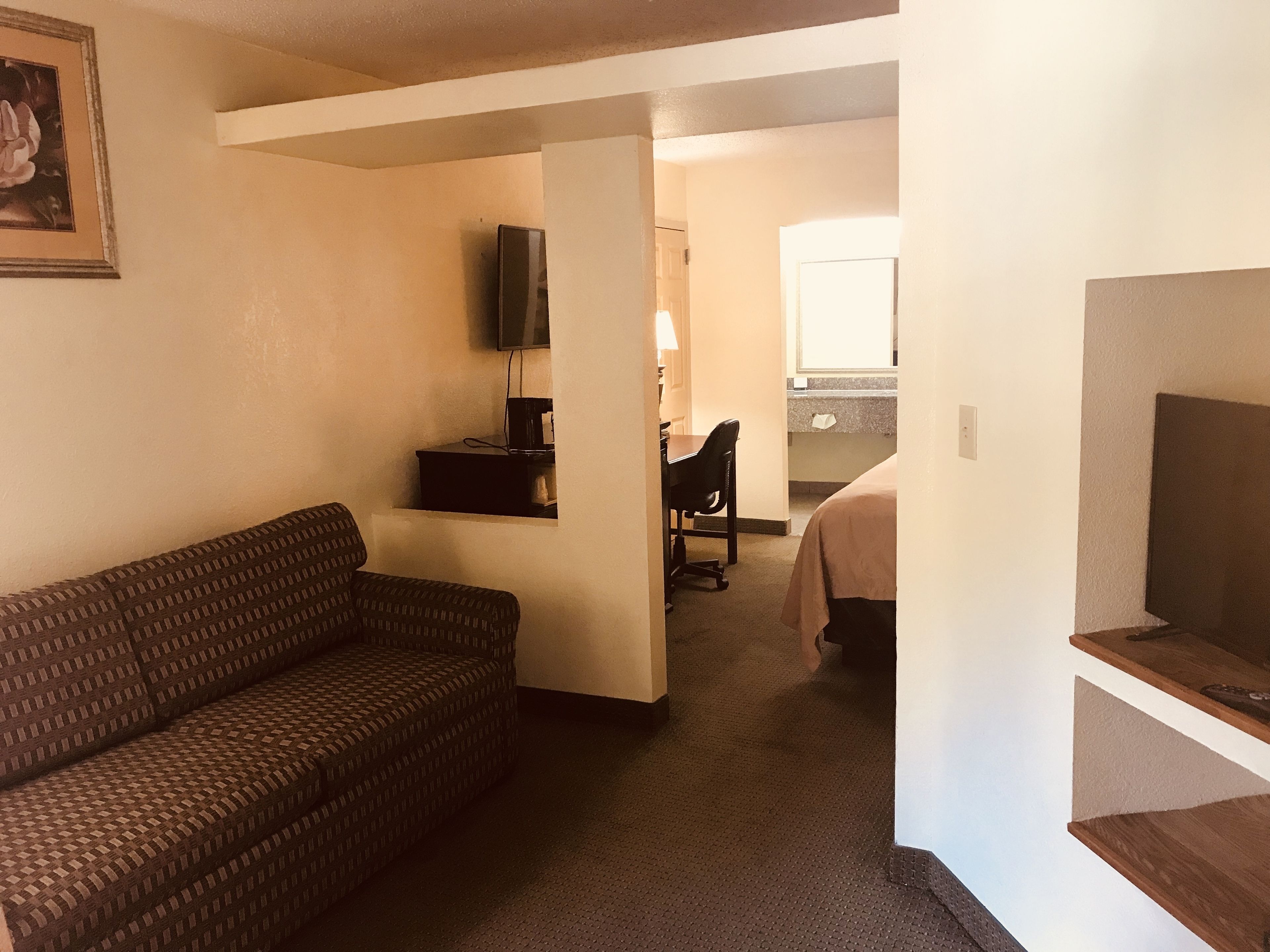 A hotel room with a sofa, a TV mounted on the wall, a desk with a computer, and a bed.