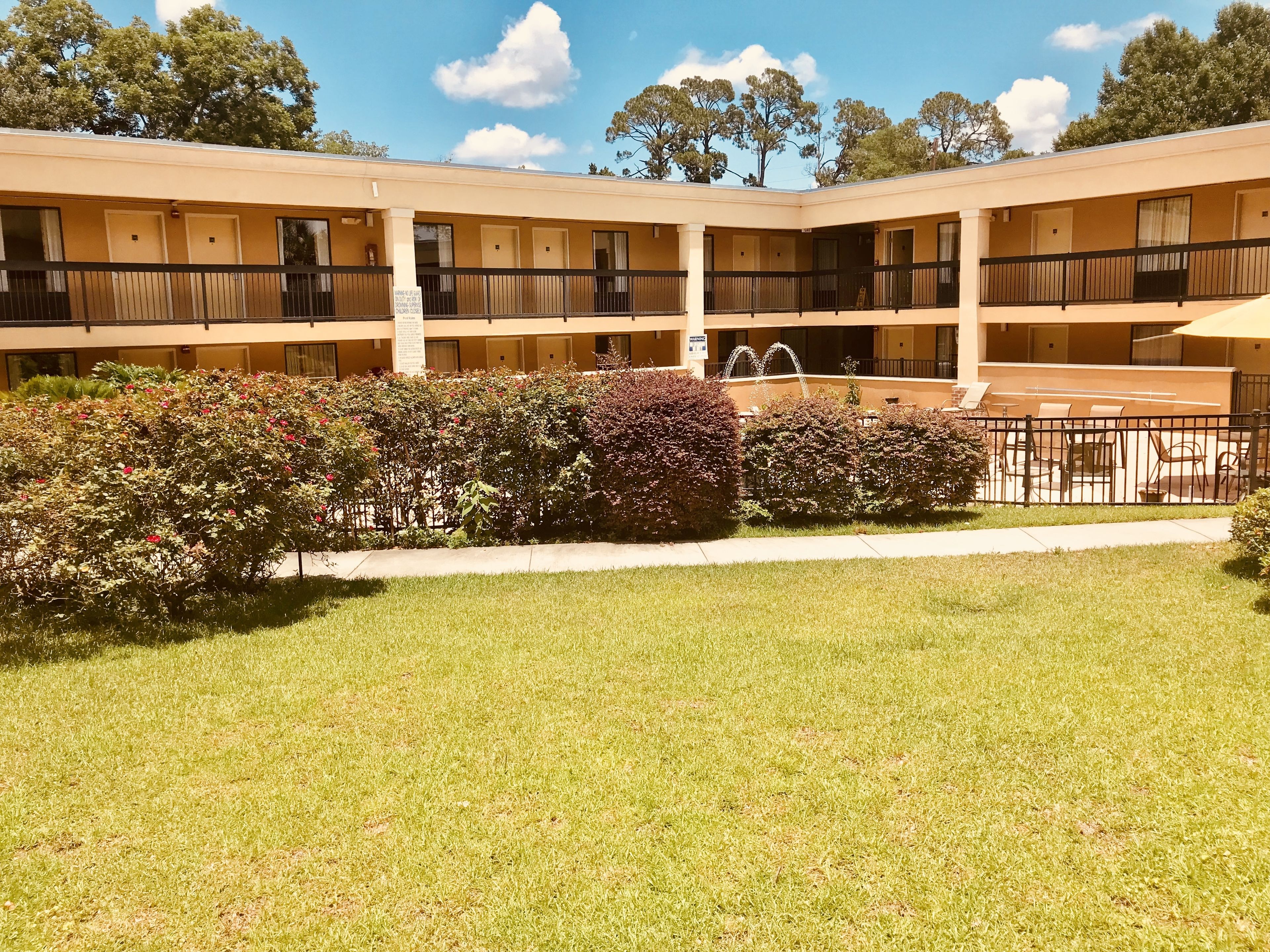 A multi-story hotel with a central courtyard, outdoor seating area, and a well-maintained lawn.