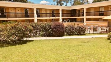 A multi-story hotel with a central courtyard, outdoor seating area, and a well-maintained lawn.
