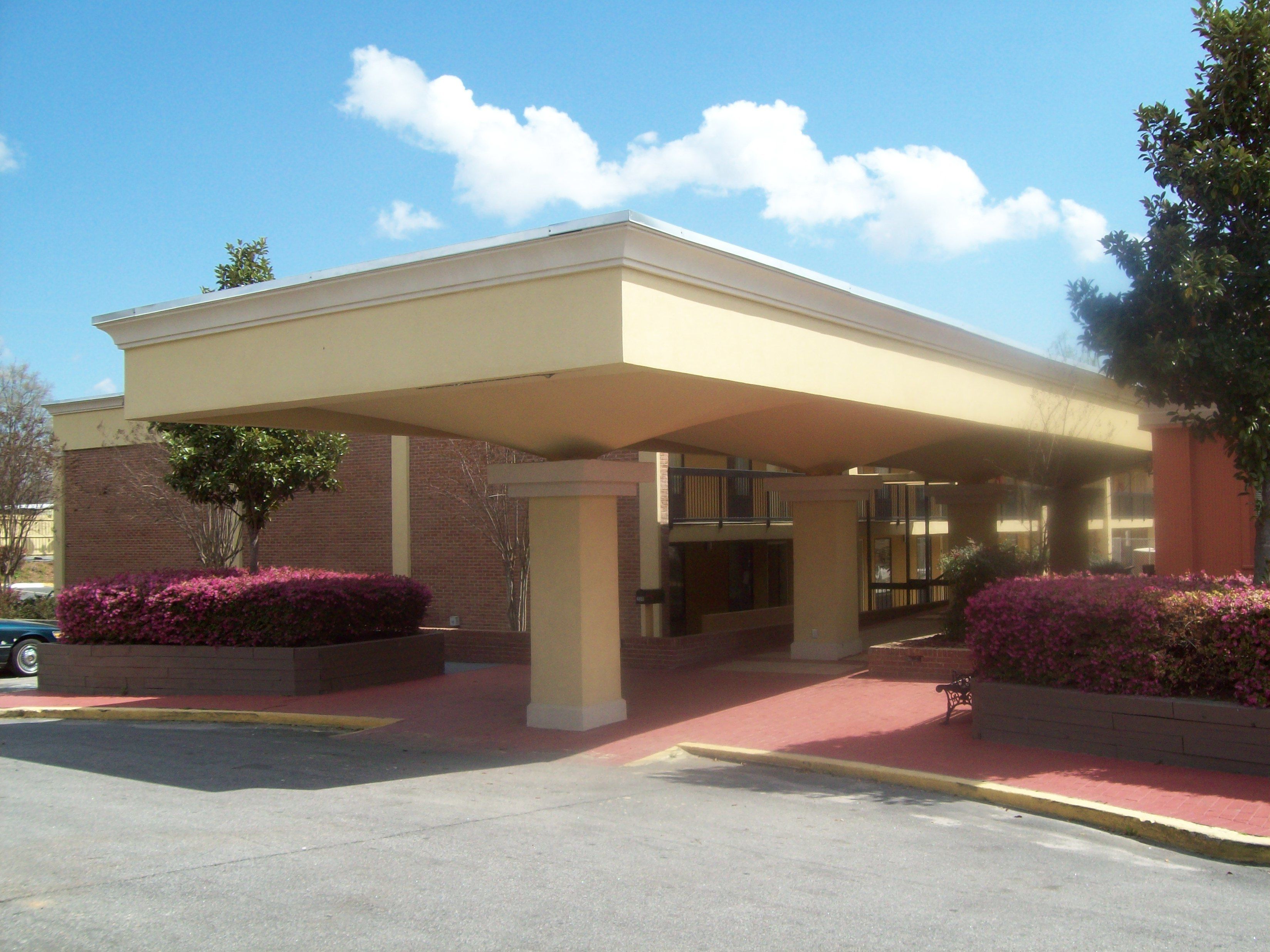 A building with a flat roof, a brick facade, and a covered entrance area with a red-paved walkway.