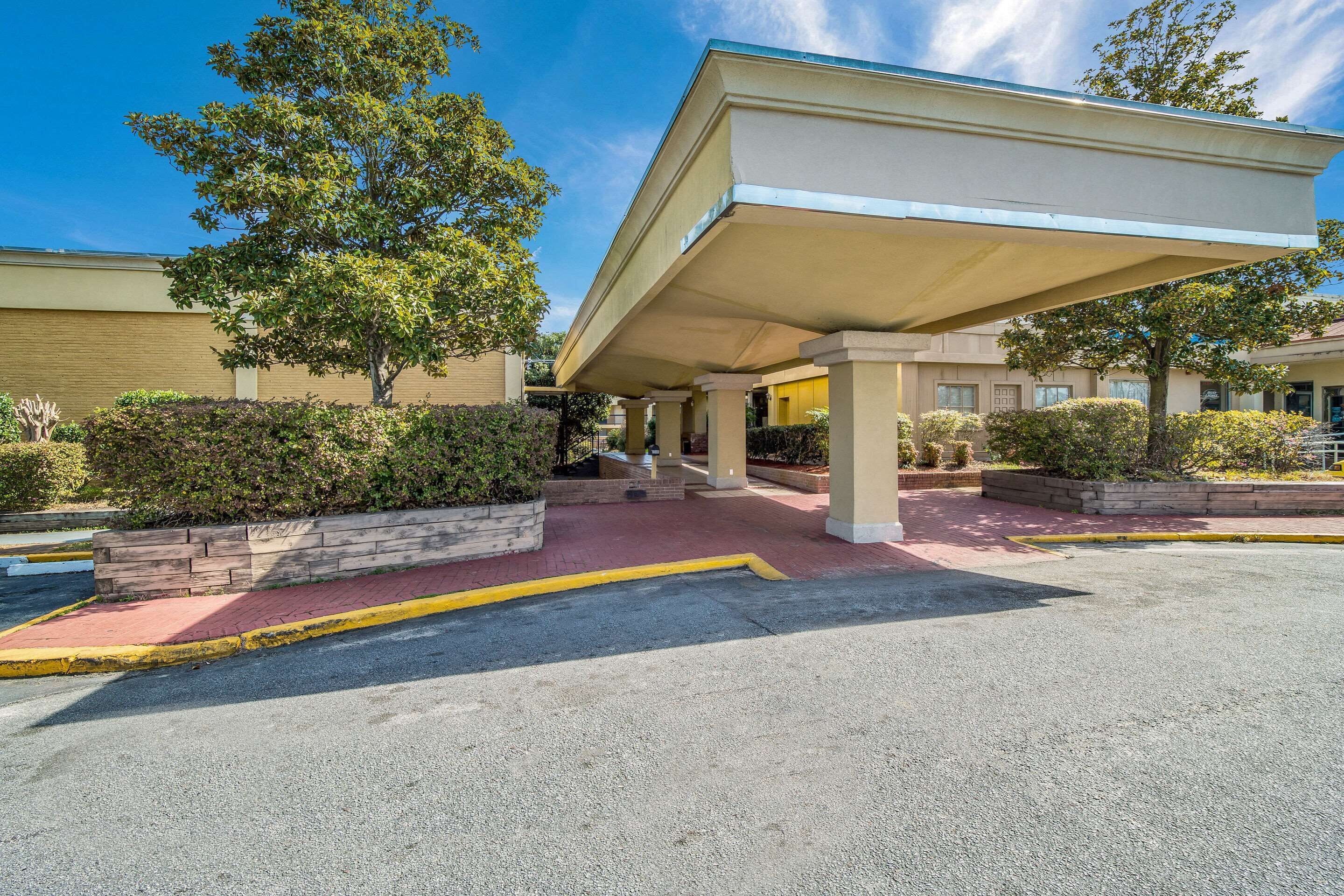 A hotel entrance with a covered walkway, a building facade, and surrounding greenery.