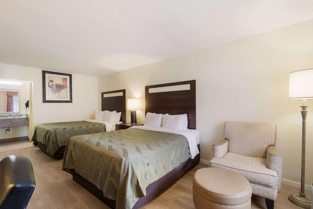 Una habitación de hotel con dos camas, una silla, un escritorio y una lámpara.