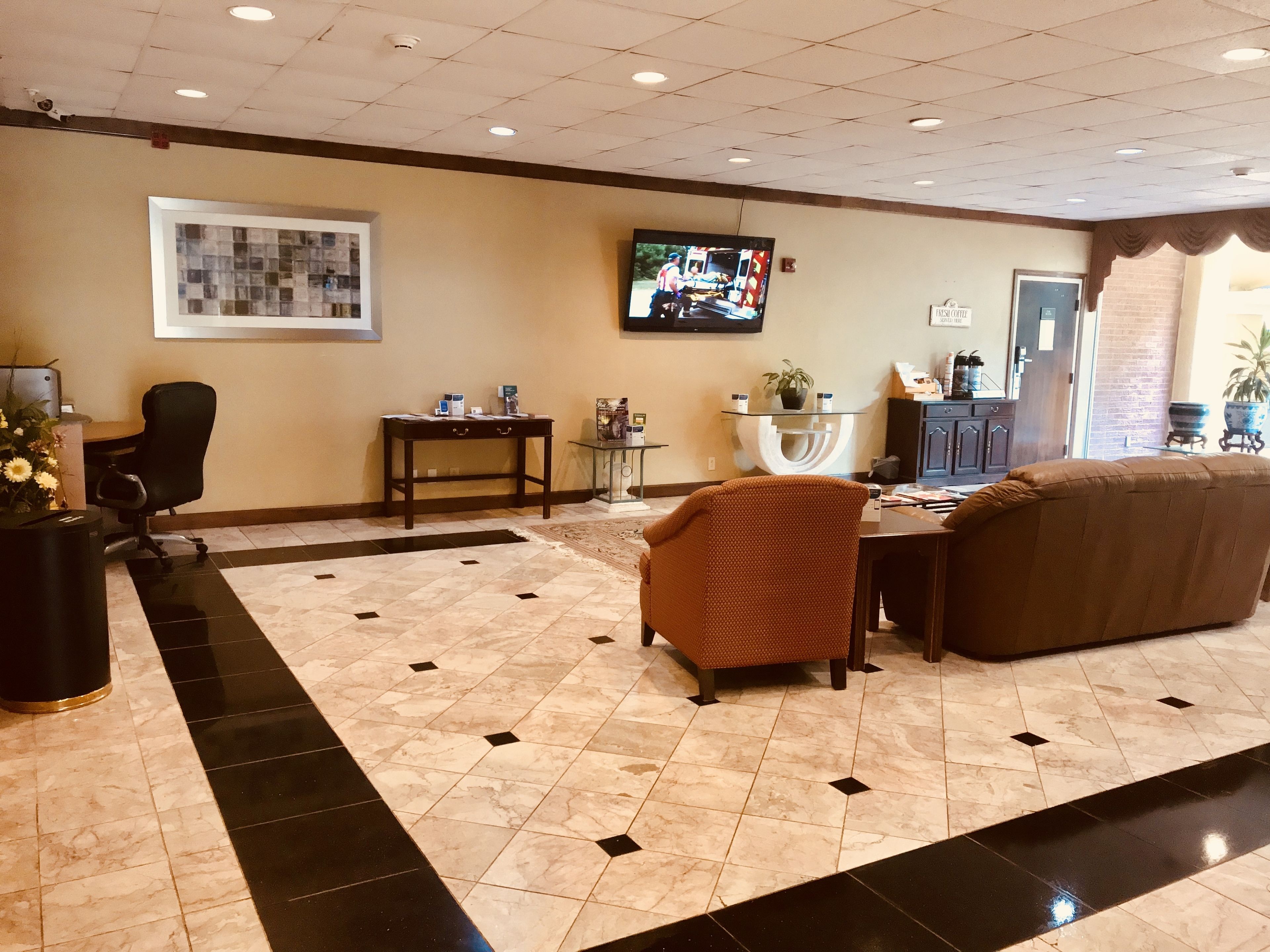 A lobby with a tiled floor, a television mounted on the wall, a reception desk, a sofa, and a potted plant.