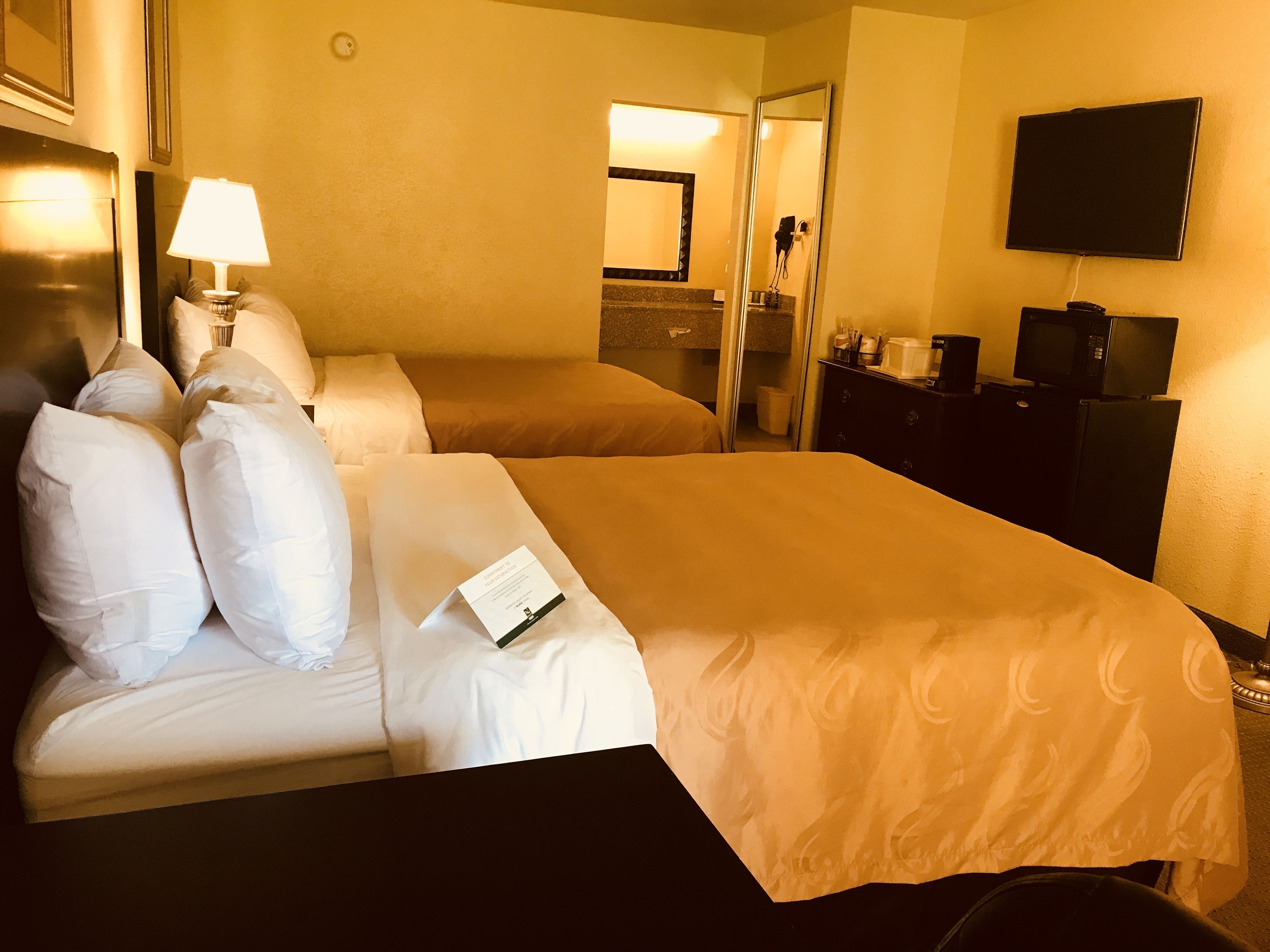 A hotel room with two beds, a desk, a mirror, a television, and a coffee maker.