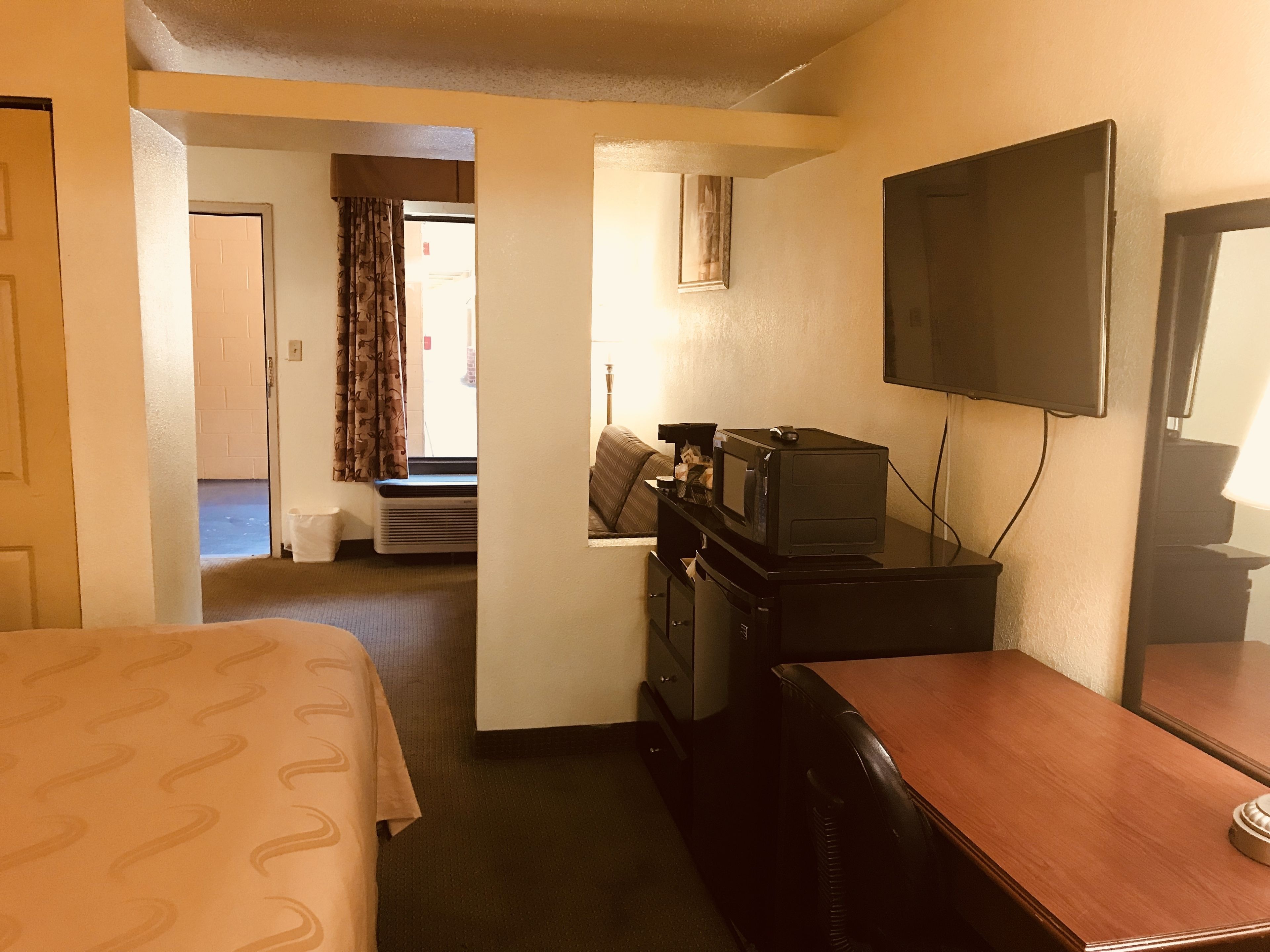 A hotel room with a bed, a desk with a television, and a window with curtains.