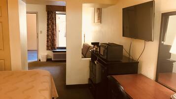 A hotel room with a bed, a desk with a television, and a window with curtains.