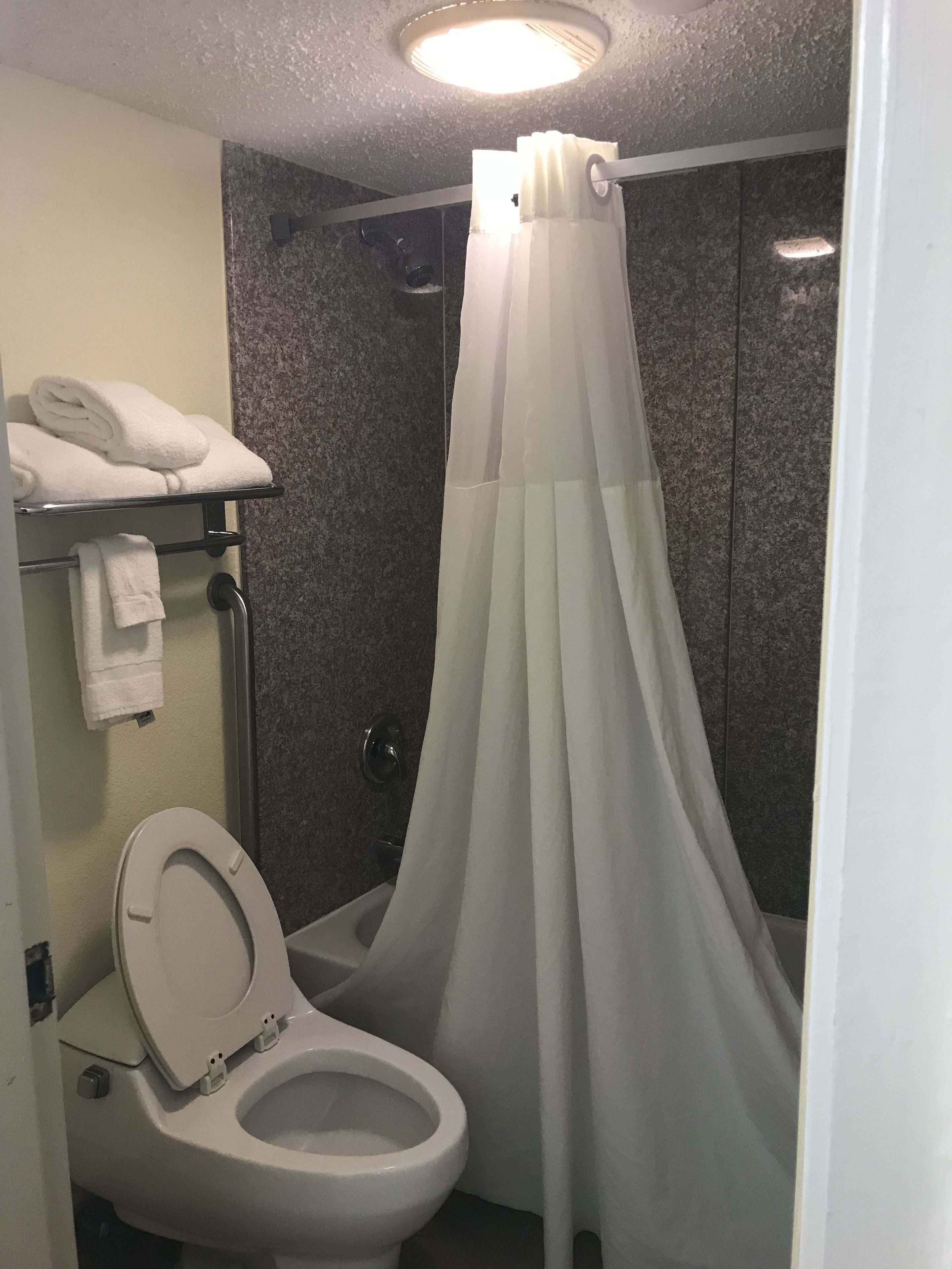 A bathroom with a toilet, a shower curtain, and a towel rack with folded towels.