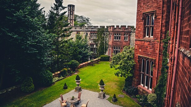 A courtyard with a lawn, stone benches, and a building with red brick walls and arched windows. - Ruthin Castle Hotel (Ruthin)