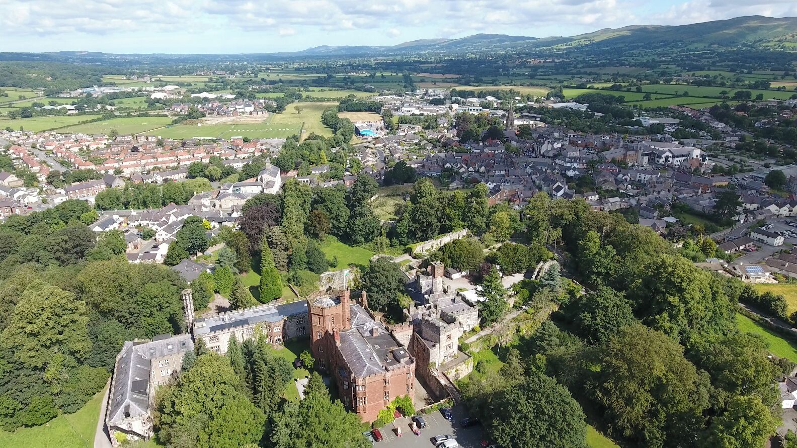 An aerial view of a town with a prominent castle-like building surrounded by greenery and residential areas.