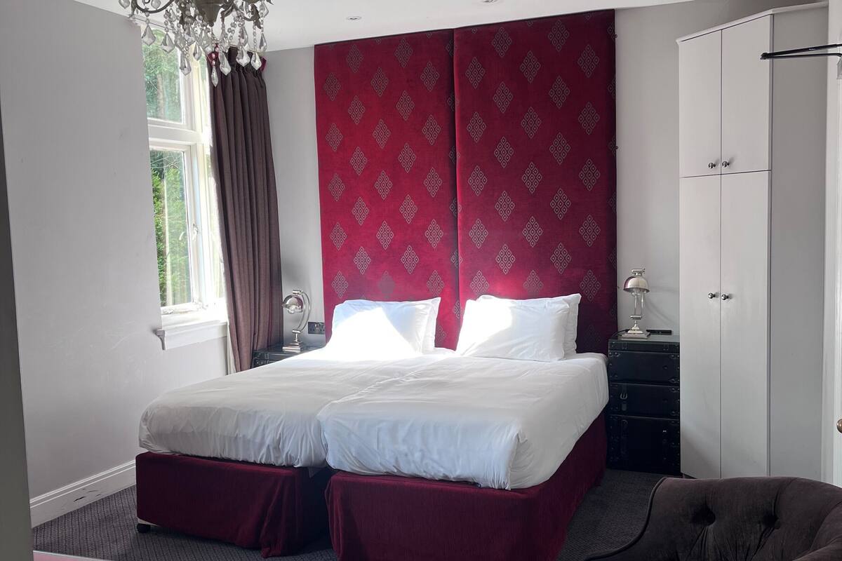A hotel room with a large bed, a wardrobe, a desk with a lamp, and a chair.