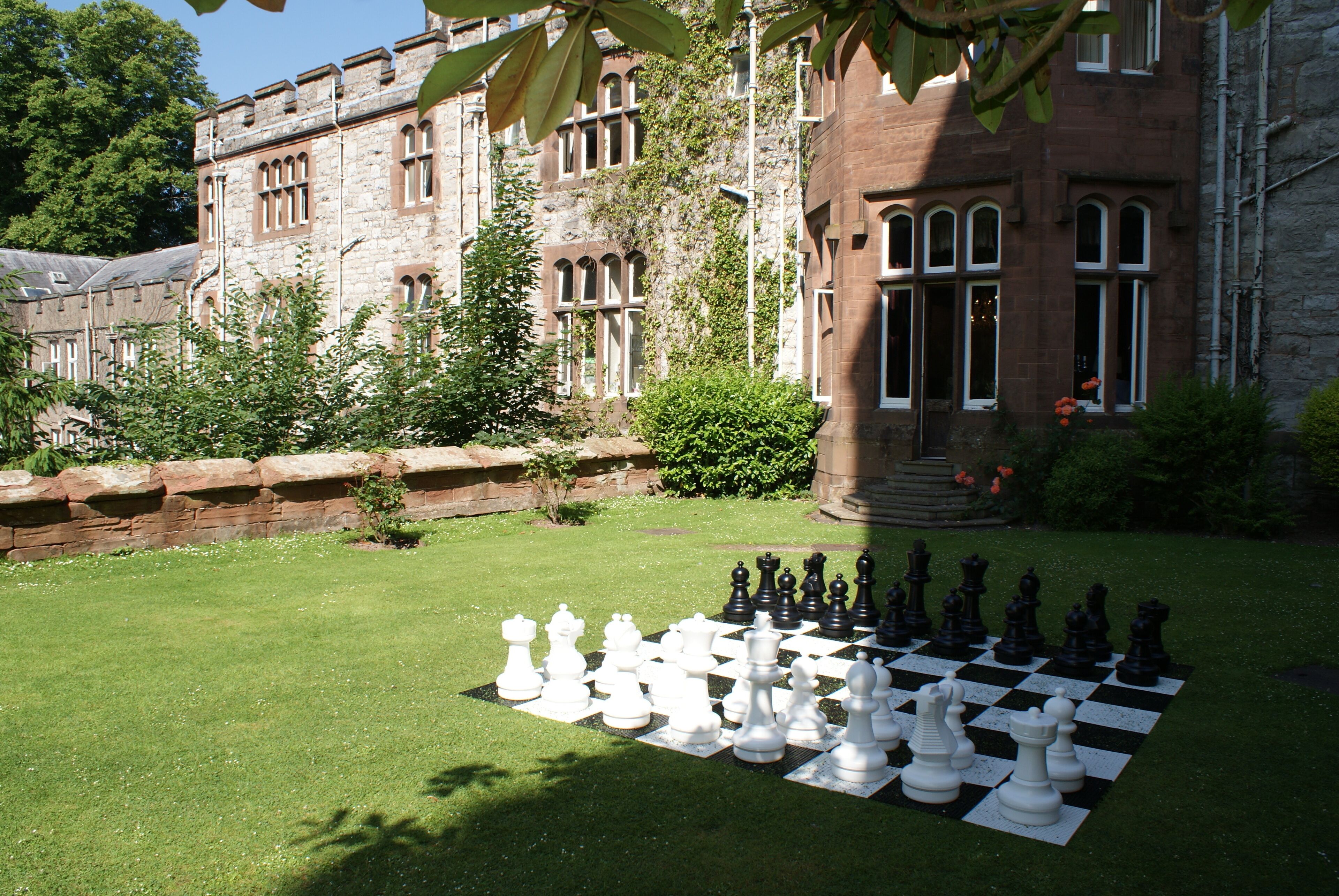 A chessboard set up on a grassy lawn in front of a historic building with stone architecture and large windows.