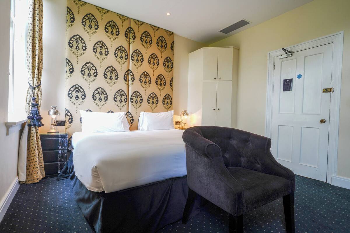 A hotel room with a bed, a chair, a wardrobe, and a door.