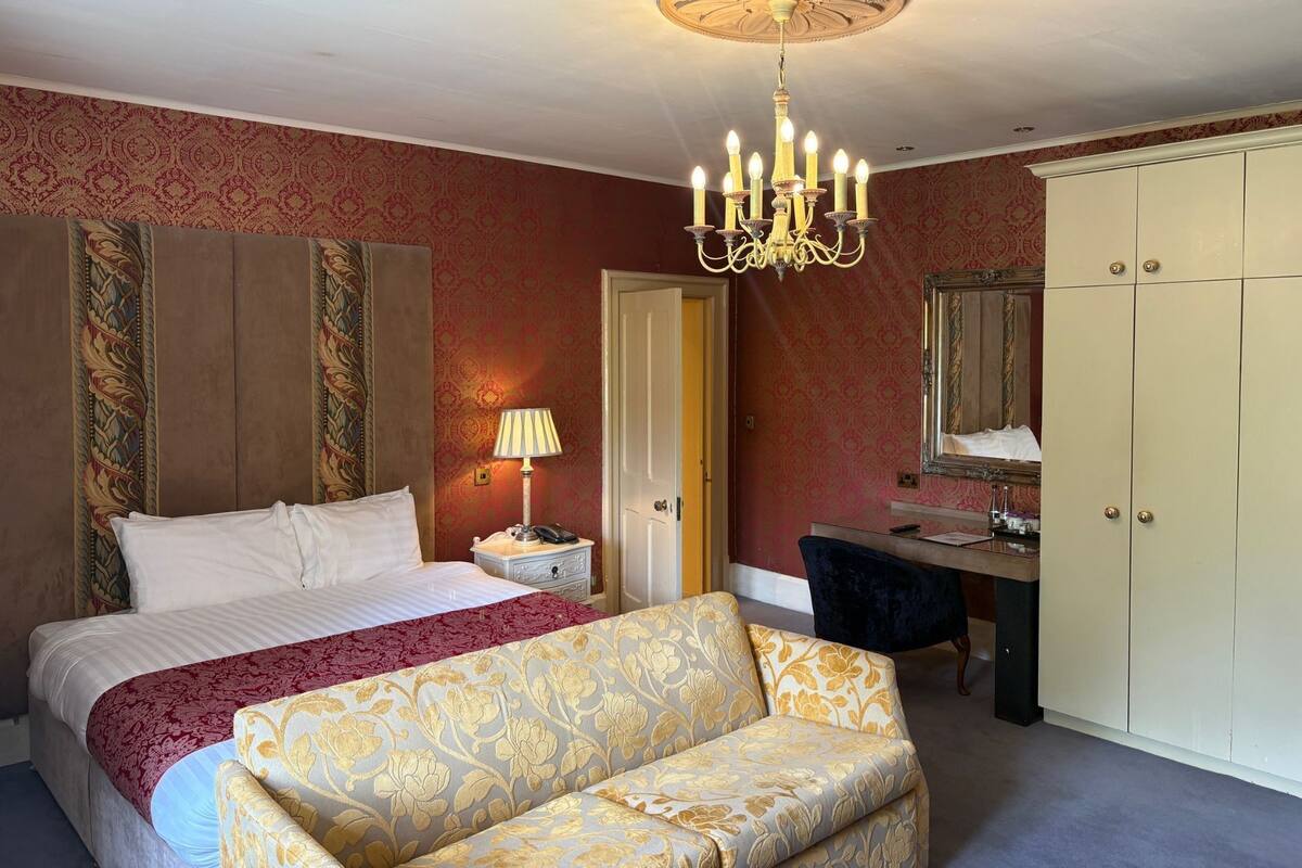 A hotel room with a bed, a desk, a chair, a wardrobe, and a chandelier.