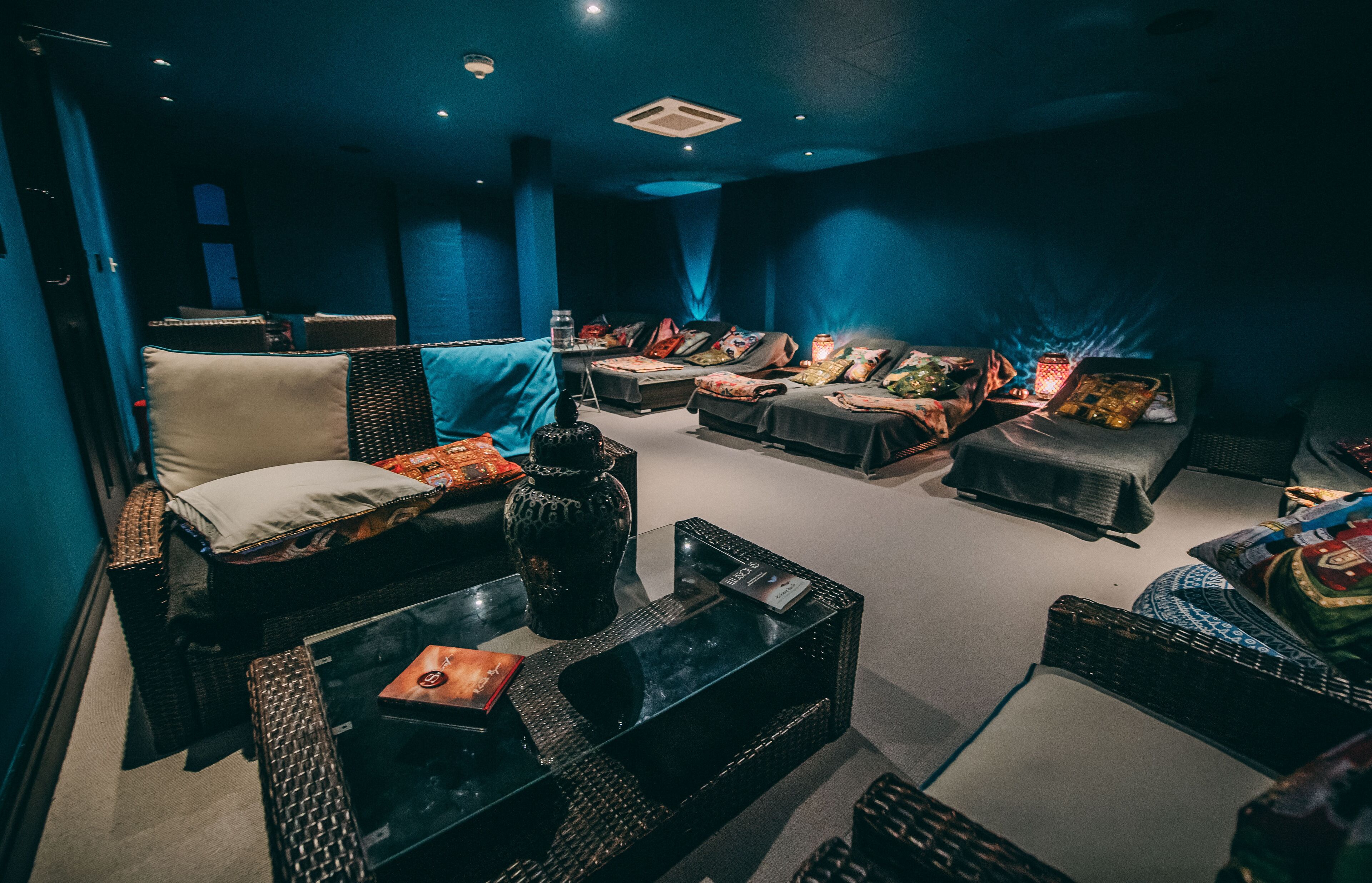 A dark-themed lounge area with seating arrangements, including sofas and chairs, and a coffee table.