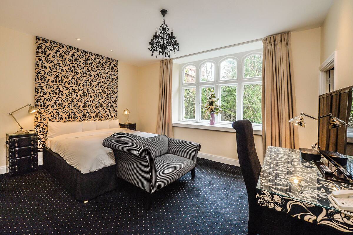 A bedroom with a bed, a sofa, a desk, and a window with curtains.