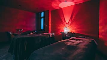 Una habitación tenuemente iluminada con dos camillas de masaje, un ventanal y una fuente de luz roja.