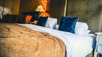 A neatly made bed with a white and brown blanket, a lamp, and a patterned wall.