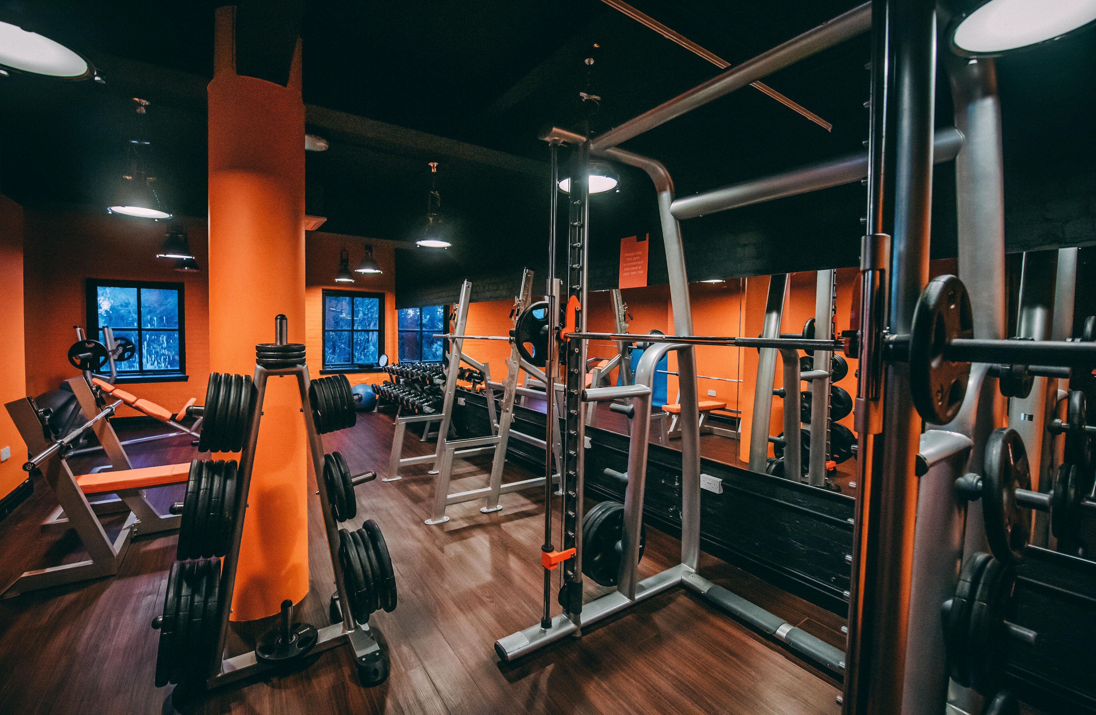 A gym with various weightlifting equipment, wooden flooring, and orange walls.