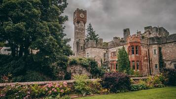 A historic castle with a prominent tower, lush greenery, and a well-maintained garden.