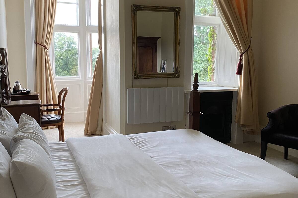 A spacious bedroom with a large bed, a wooden dresser, a chair, and a fireplace.