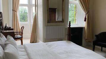 A spacious bedroom with a large bed, a wooden dresser, a chair, and a fireplace.