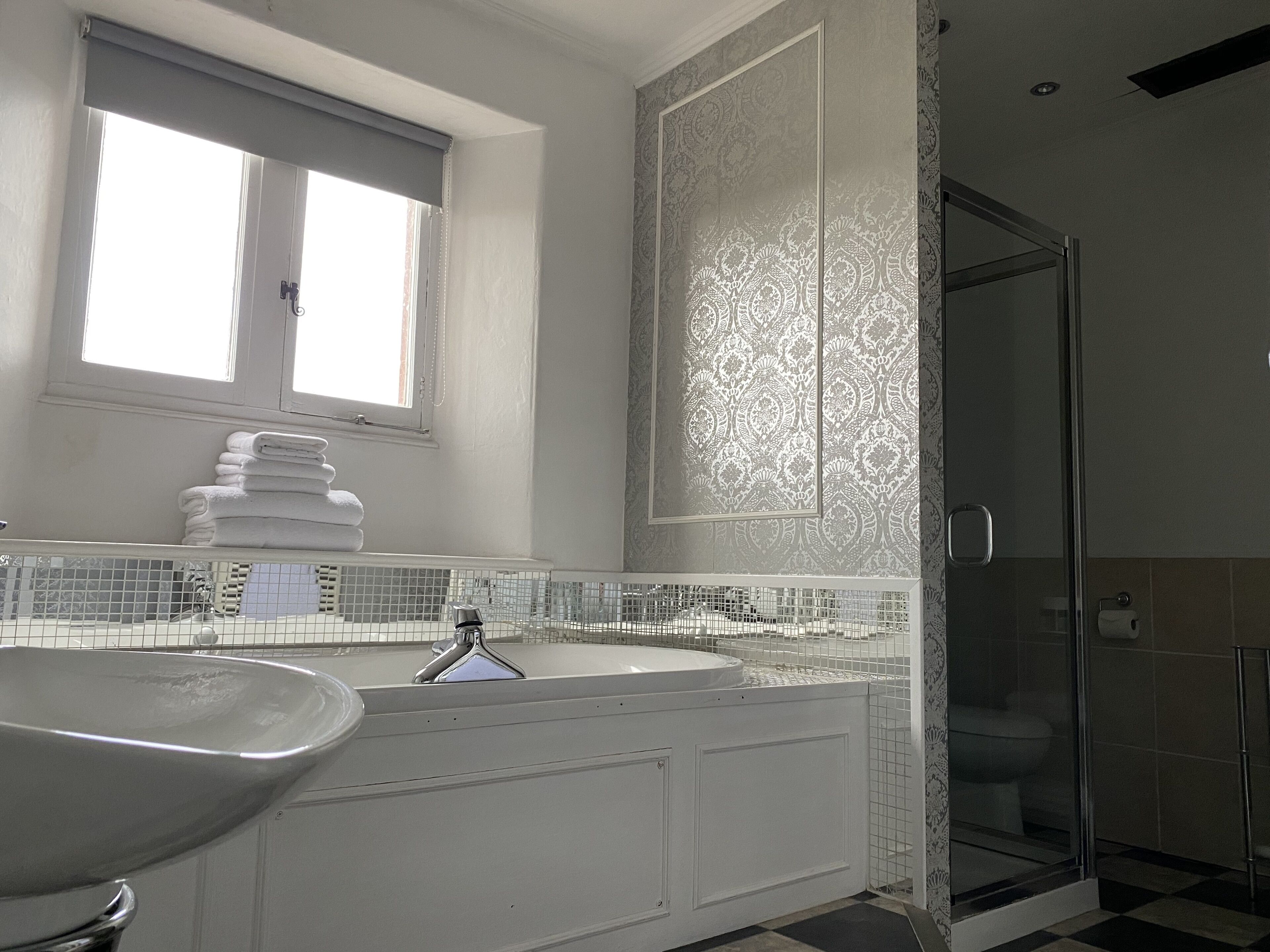 A bathroom with a large sink, a mirror, a window, and a shower area.