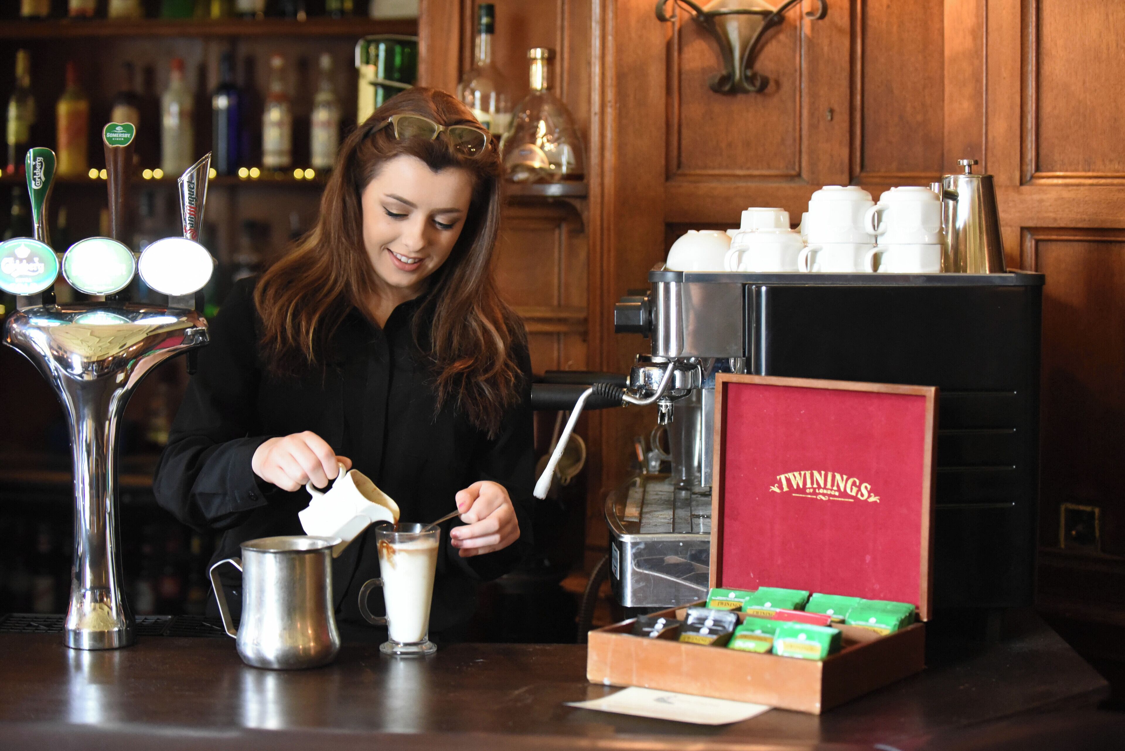 A barista preparing a drink at a coffee machine with a box of Twinings tea.