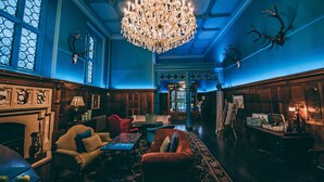 A room with a chandelier, wooden paneling, a fireplace, and a large window with stained glass. - Ruthin Castle Hotel (Ruthin)