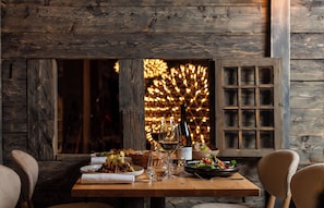 A wooden dining table set with plates of food, wine glasses, and a bottle of wine.
