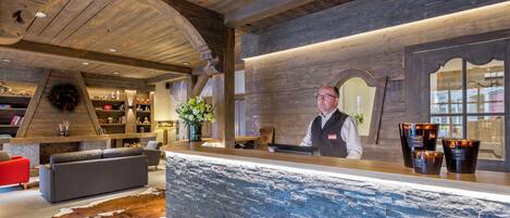 Een receptie met een houten plafond, een stenen muur en een receptiemedewerker.