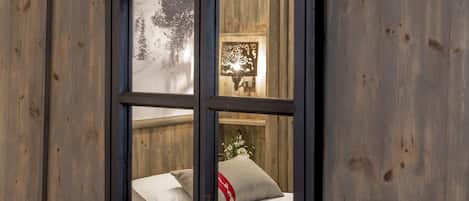A window with a view of a bed and a wall with a decorative panel.