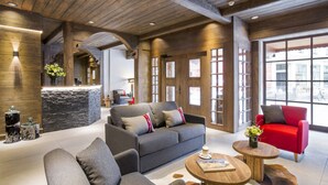 Un interior moderno con un sofá gris, un sillón rojo, techo de madera, pared de acento de piedra y ventanas amplias.