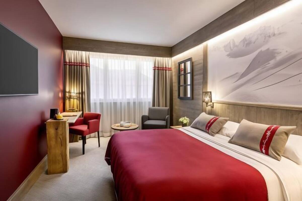 A hotel room with a large bed, a desk, a chair, and a window with curtains.