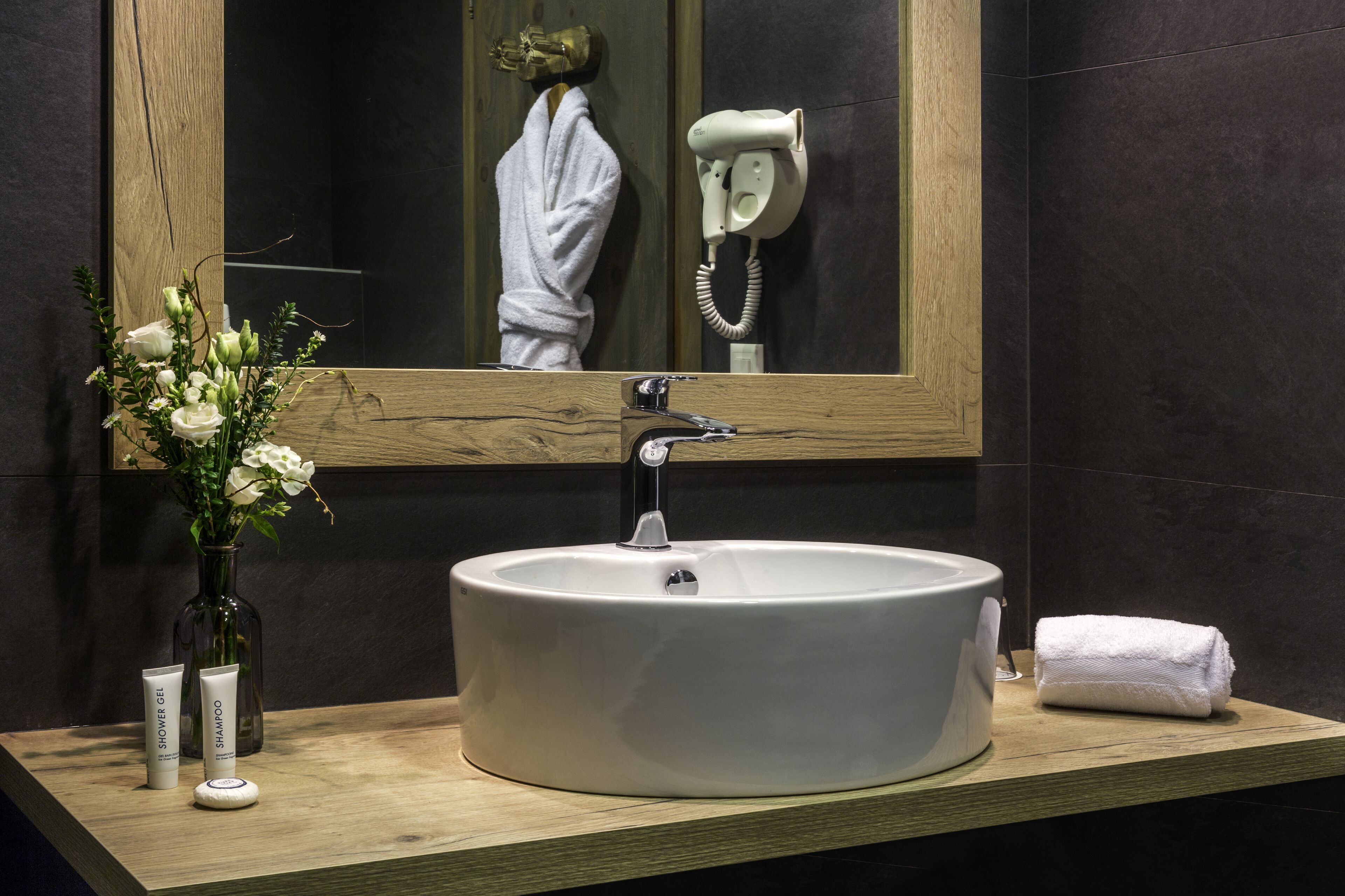 Une salle de bain avec un grand lavabo ovale, un miroir, un sèche-cheveux et des articles de toilette posés sur le comptoir.