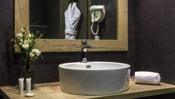 Une salle de bain avec un grand lavabo ovale, un miroir, un sèche-cheveux et des articles de toilette posés sur le comptoir.