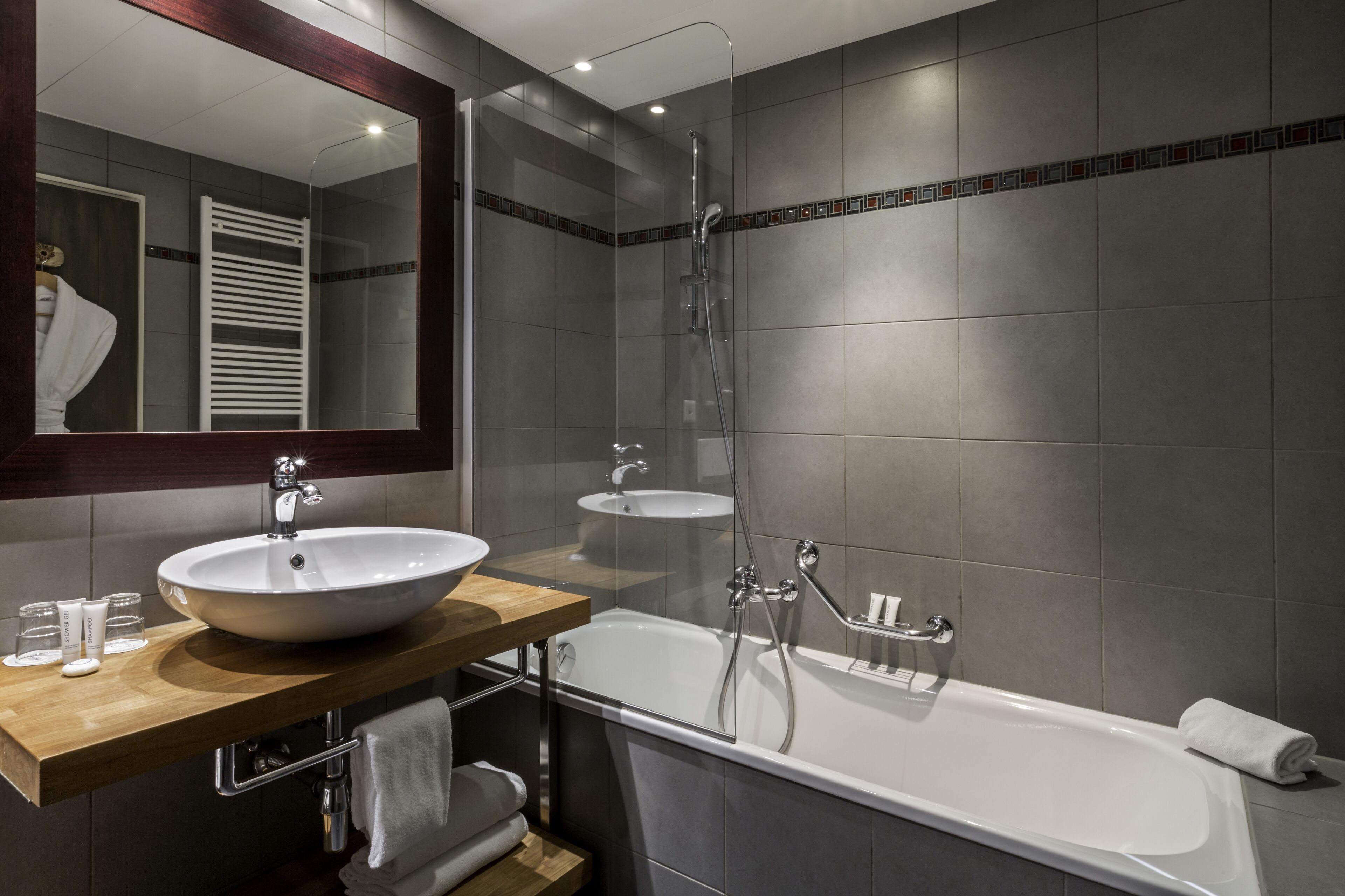 A modern bathroom with a large mirror, two sinks, a bathtub, and a shower.