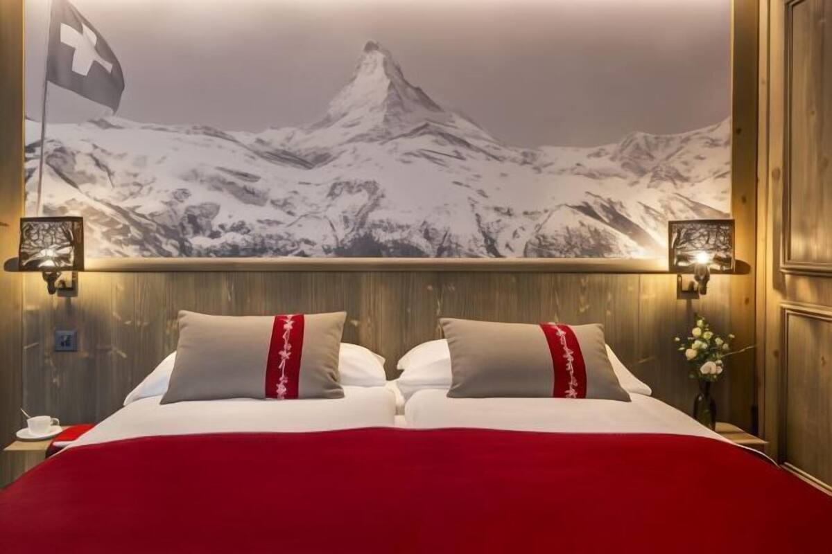 A hotel room with a bed, a large wall mural of a mountain, and two wall-mounted lamps.