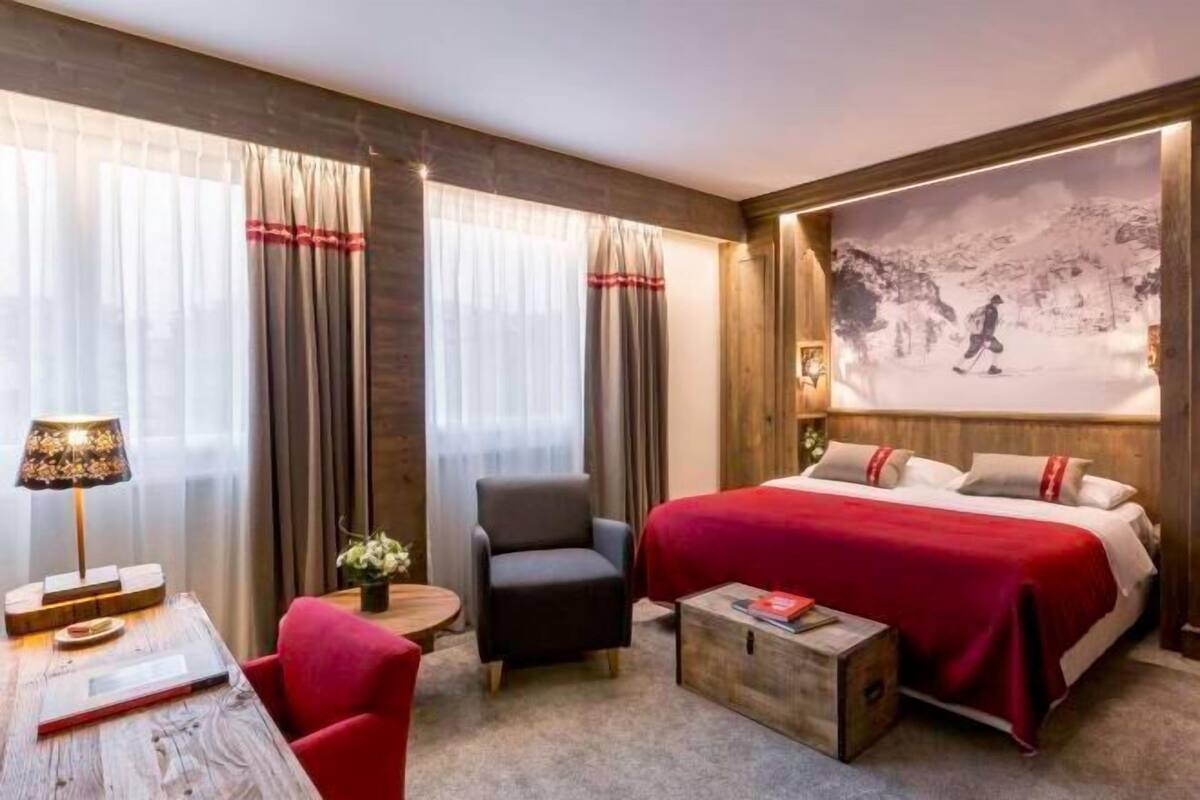 A hotel room with a bed, a chair, a table, and a wall-mounted painting.