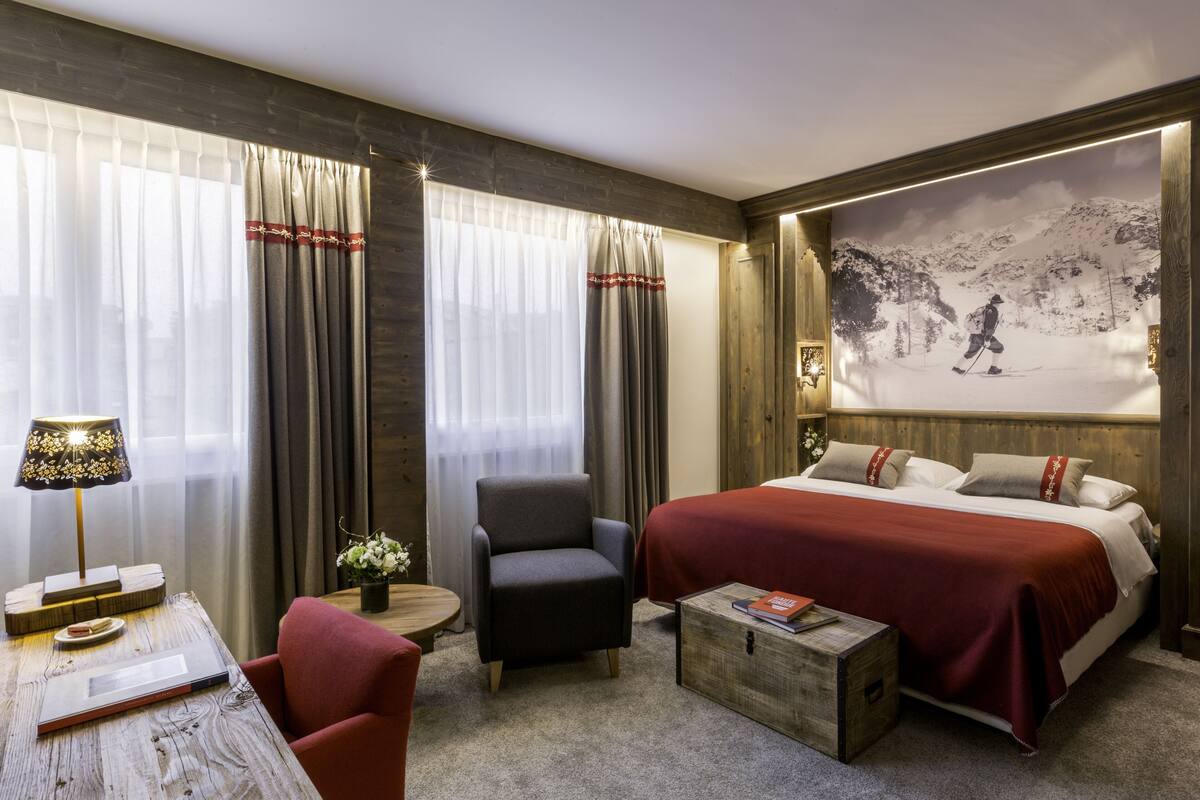A hotel room with a large bed, a desk with a lamp, a chair, and a painting on the wall.
