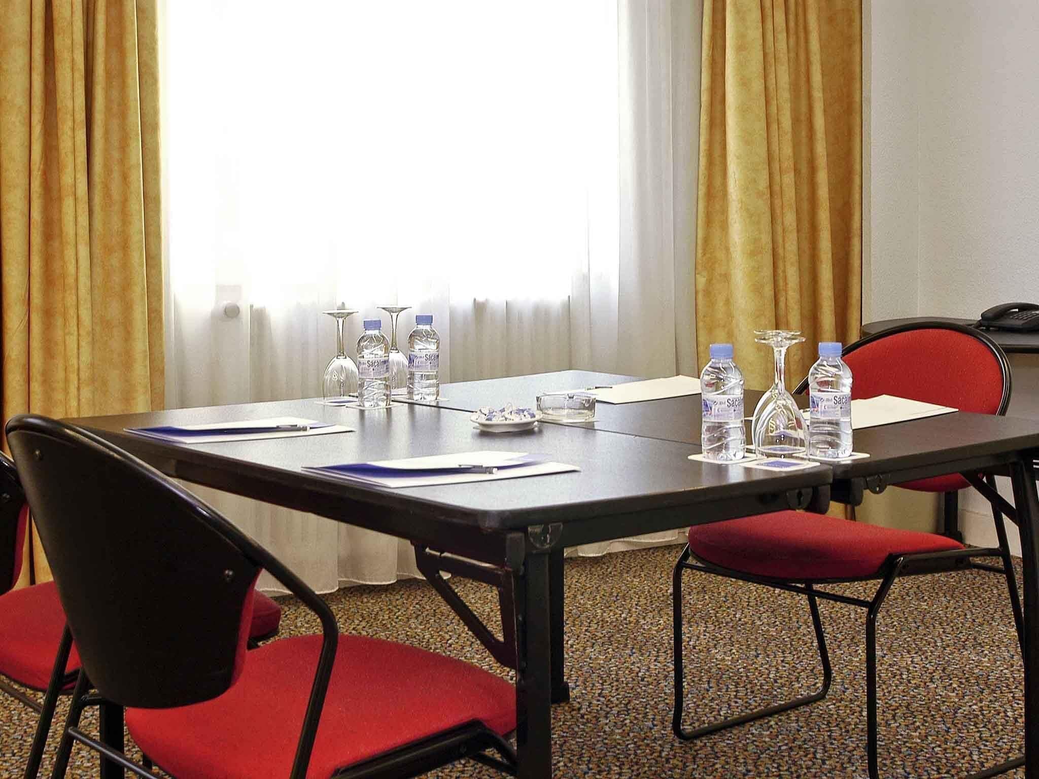 Un salón de conferencias con una mesa, sillas, botellas de agua y documentos.
