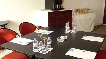 Uma sala de conferências com uma mesa de madeira escura, cadeiras vermelhas, garrafas de água e uma máquina de café.