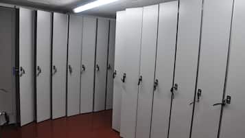 A row of white lockers with metal handles, a red floor, and a fluorescent light fixture on the ceiling.